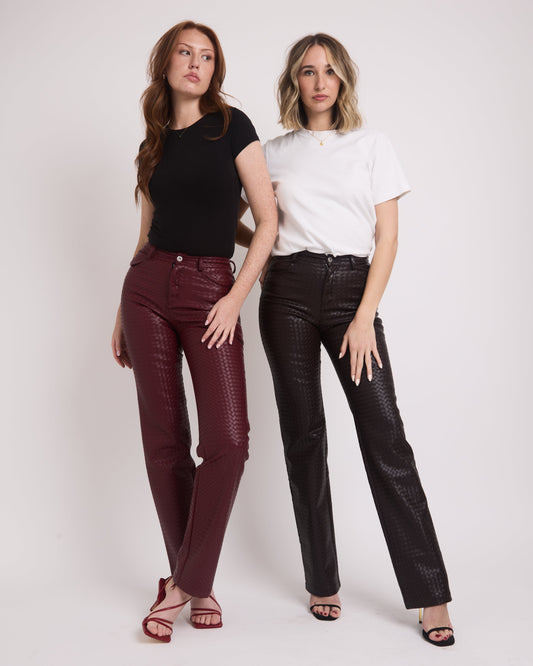 Two tall girls standing on a grey backdrop wearing tall leather trousers