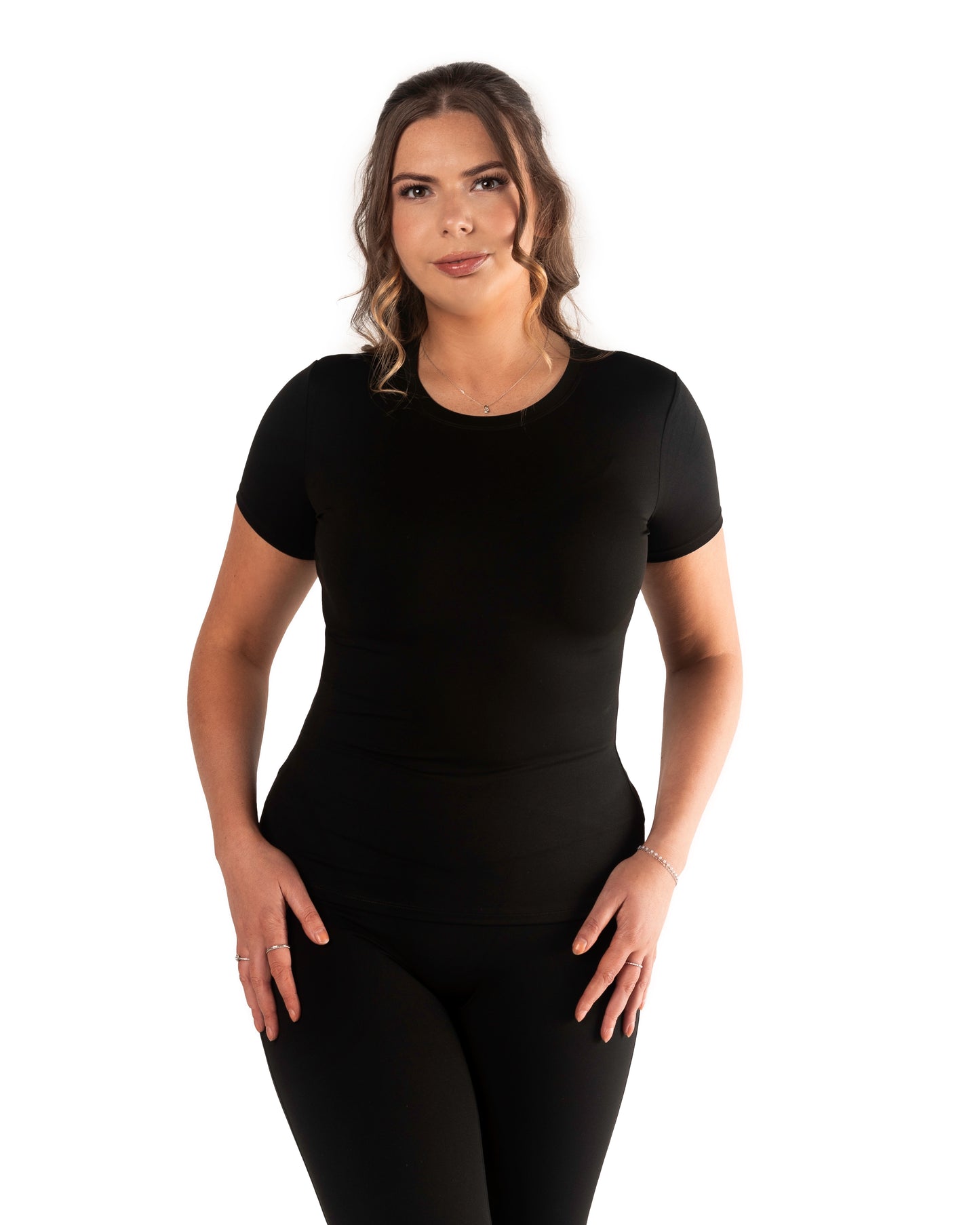 A model wearing a tall short sleeve active t-shirt in black color, posing with hands on hips.