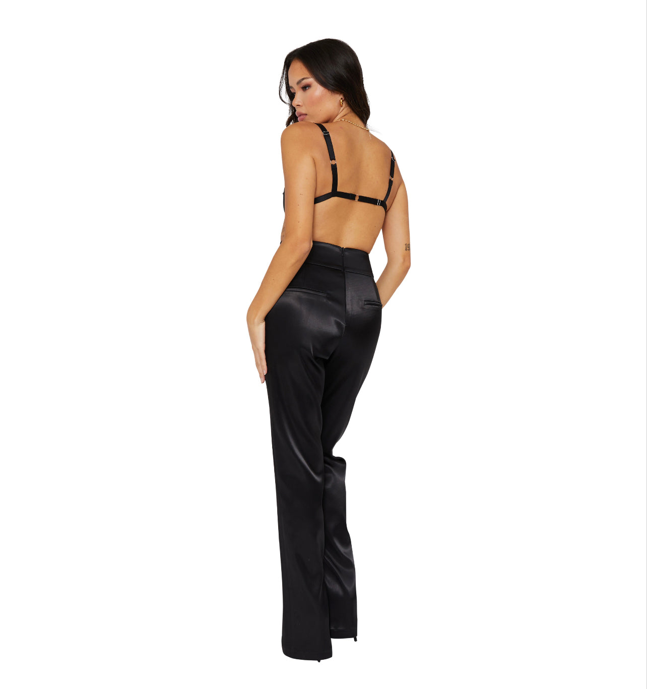 A Tall model wearing high waisted satin trousers with a straight leg cut, featuring a back zip and hook closure, and leg zip detailing. standing to the back with two pockets at the back.