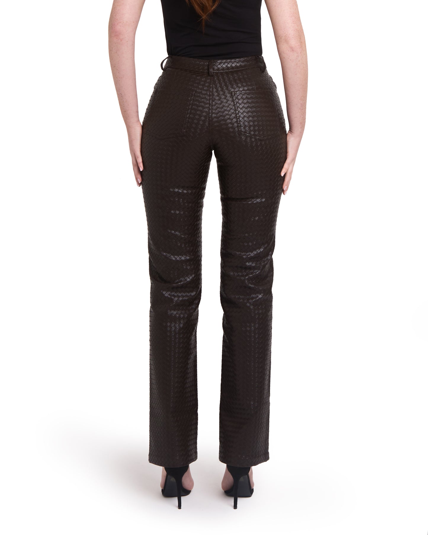 A pair of tall woven leather trousers in deep brown color, with a straight leg design. The trousers are modelled by a person standing against a plain background. Back shot