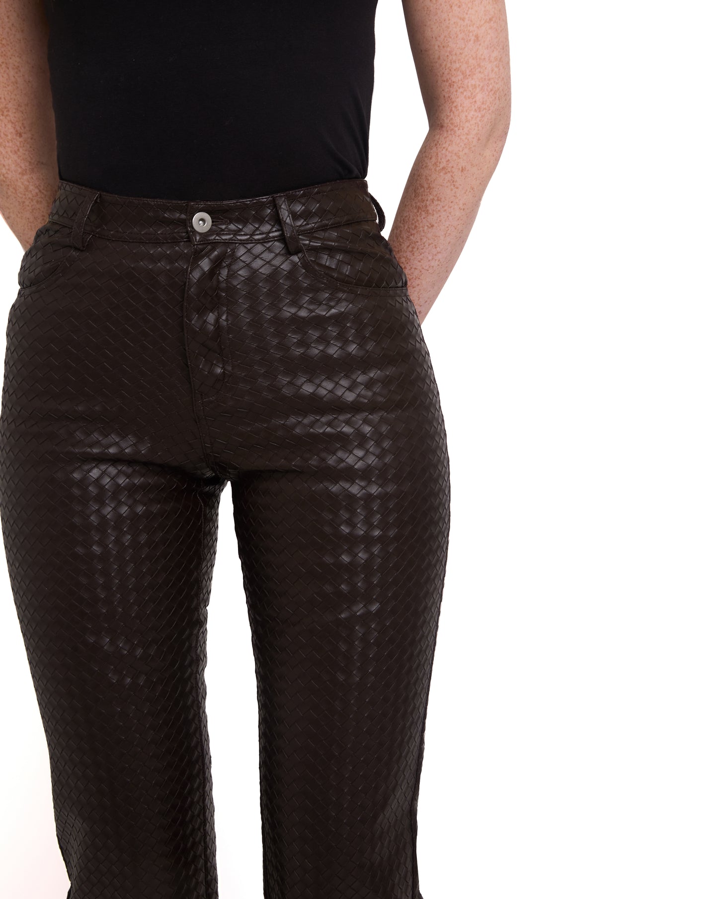 Close up of A pair of tall woven leather trousers in deep brown color, with a straight leg design. The trousers are modeled by a person standing against a plain background.