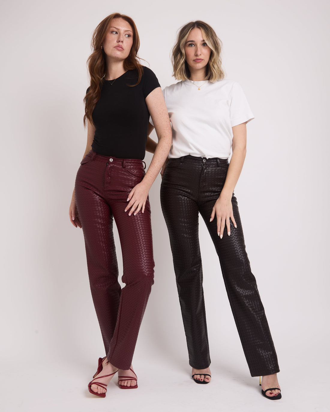 Two tall girls standing on a grey backdrop wearing tall leather trousers