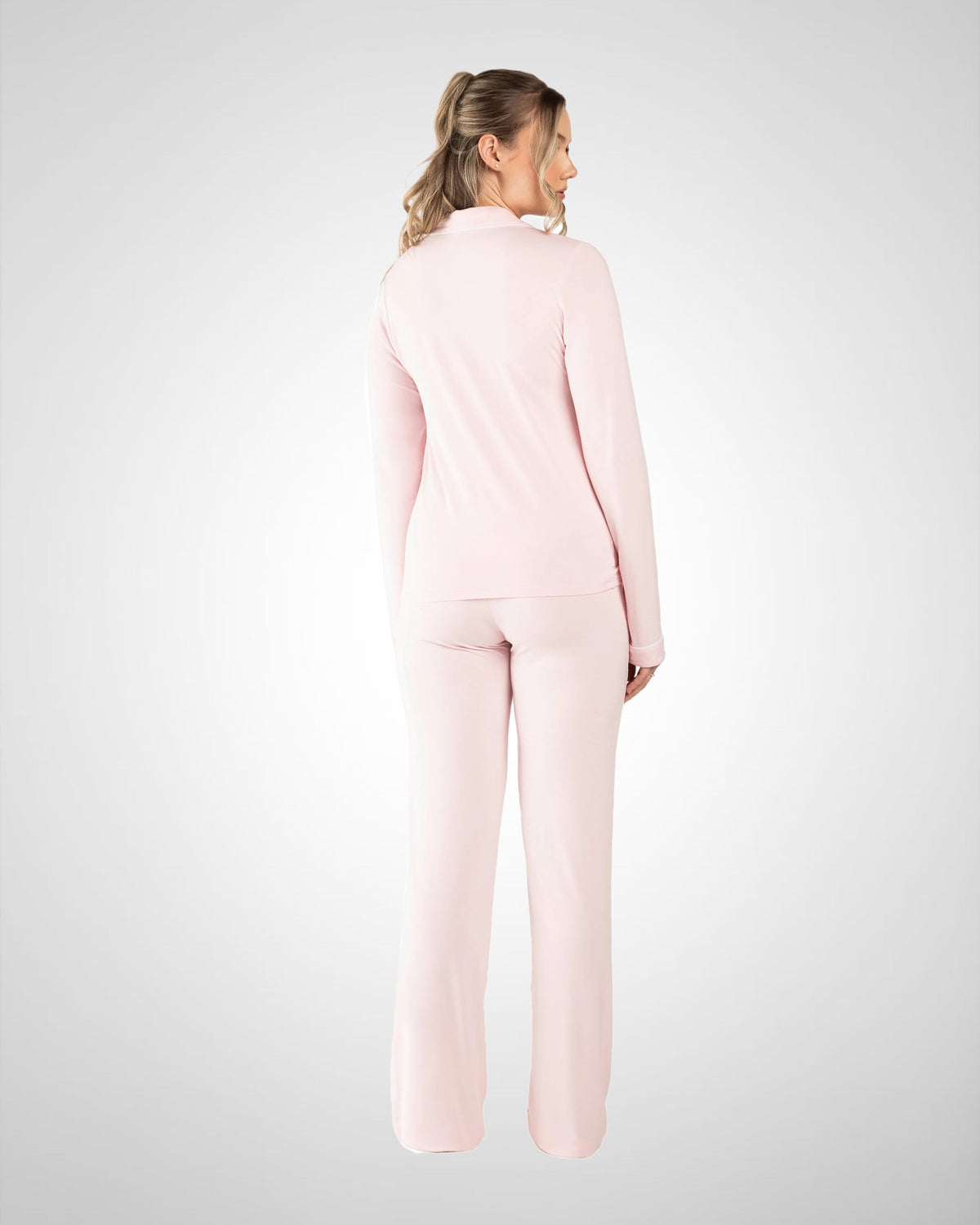 A woman wearing a light pink two-piece lounge set, viewed from the back, standing against a light gray studio background.
