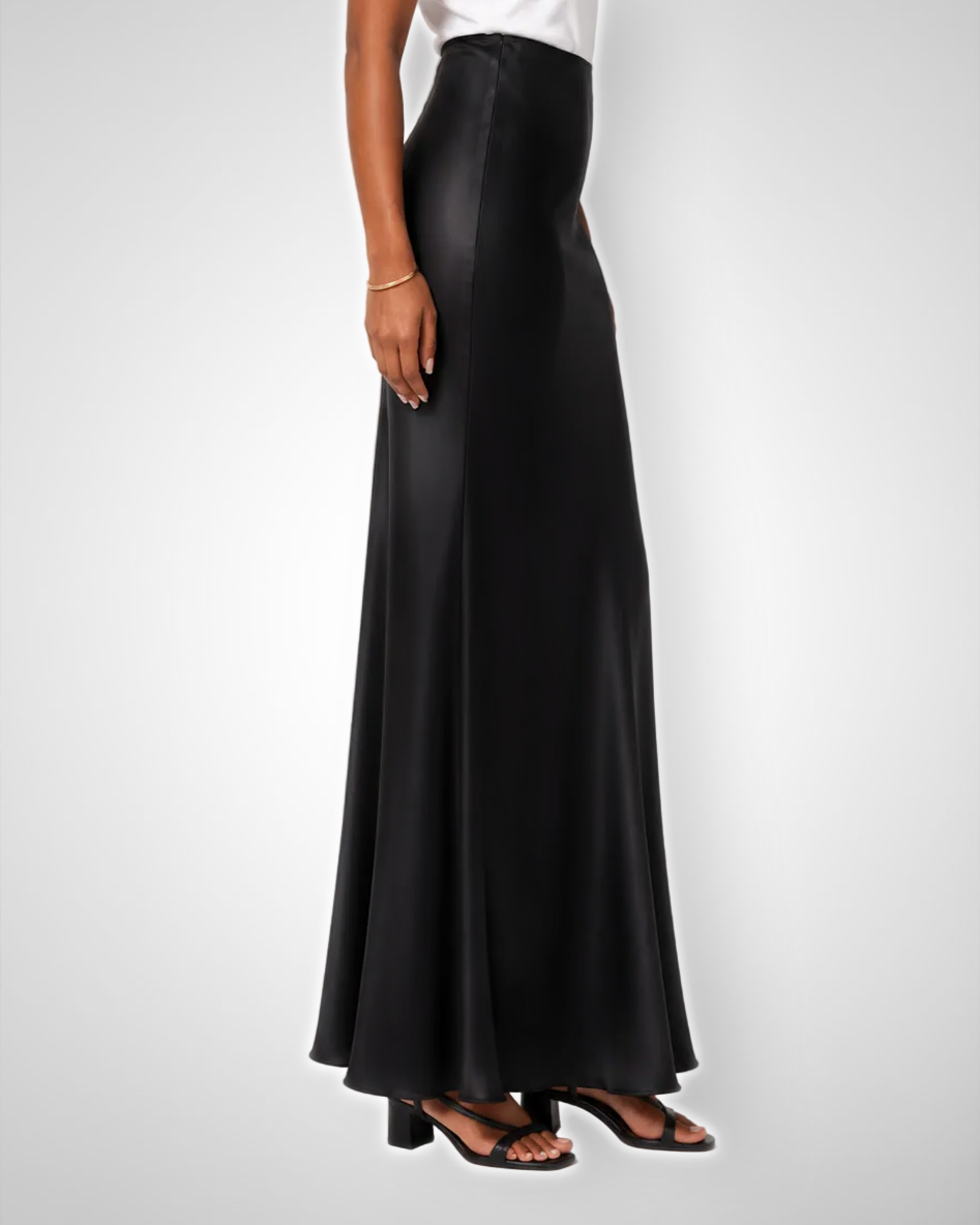 A model wearing a high-waisted, floor-length black MAXI  satin skirt with a white top and black block-heel sandals, shown from the waist down against a light gray studio background.