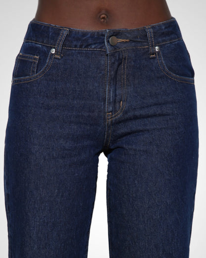 A close-up of a person wearing dark blue denim jeans against a light gray studio background.