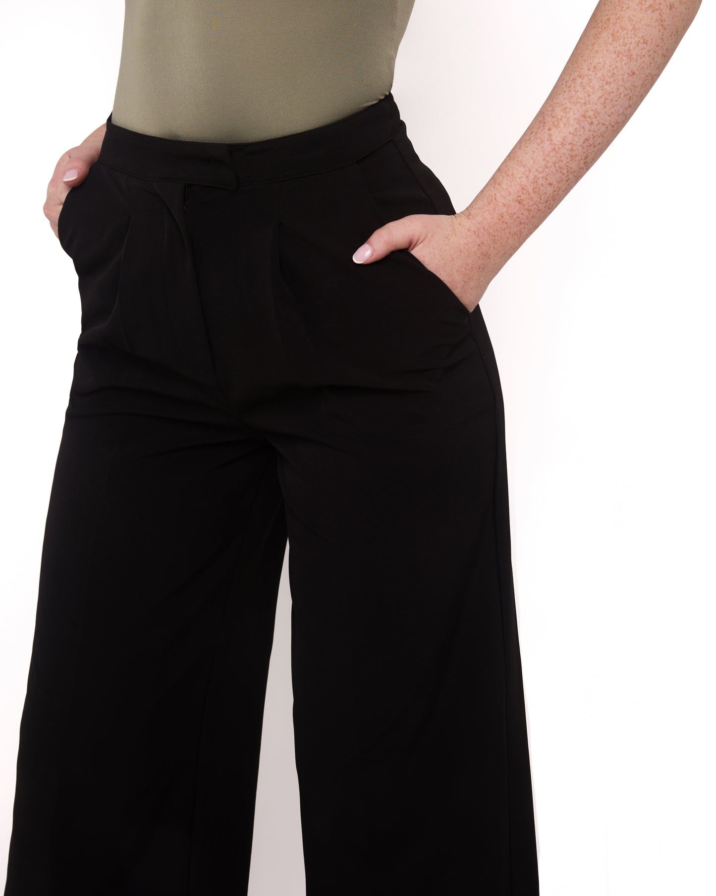 A model wearing tall wide leg tailored trousers in black with a high-waisted fit and a sleek silhouette. Close up shot with hands in pocket 