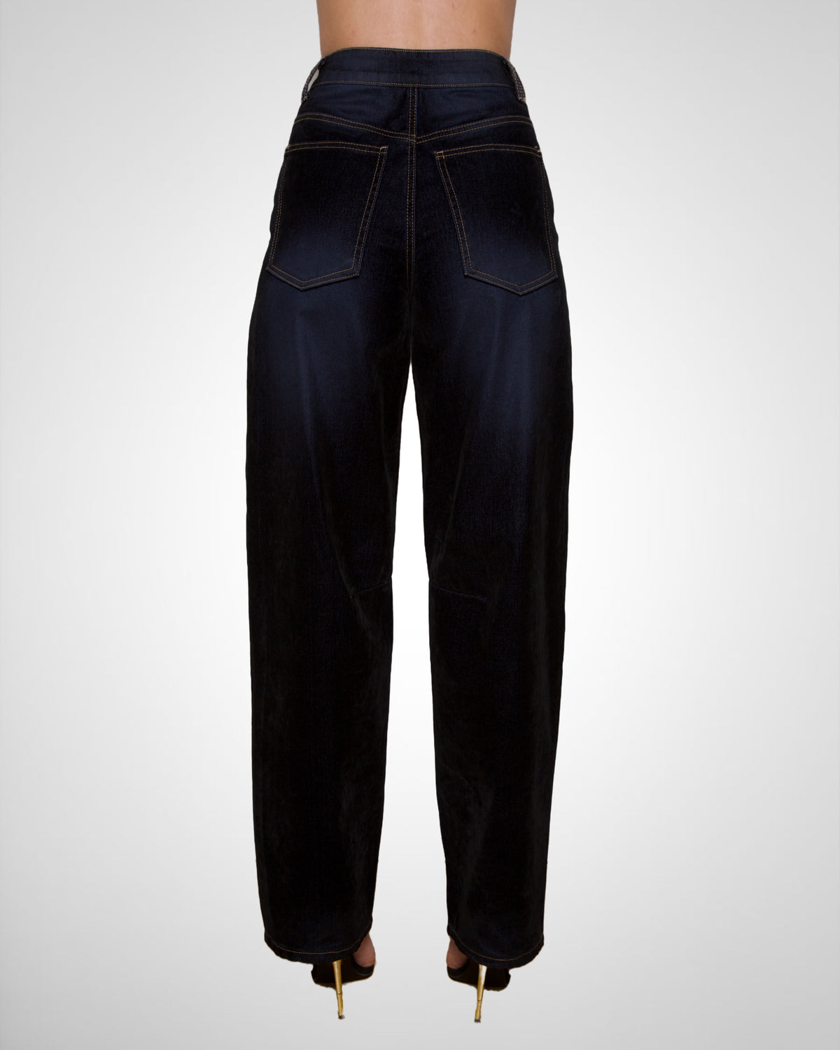 Rear view of a tall model wearing dark indigo high-waisted wide-leg jeans with gold-tone heels, shown against a light gray studio background.