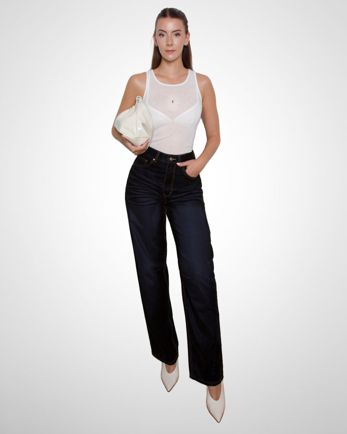 A tall woman modeling a white semi-sheer sleeveless top, dark navy wide-leg jeans, and white pointed-toe heels, holding a cream-colored clutch against a plain light gray studio background.