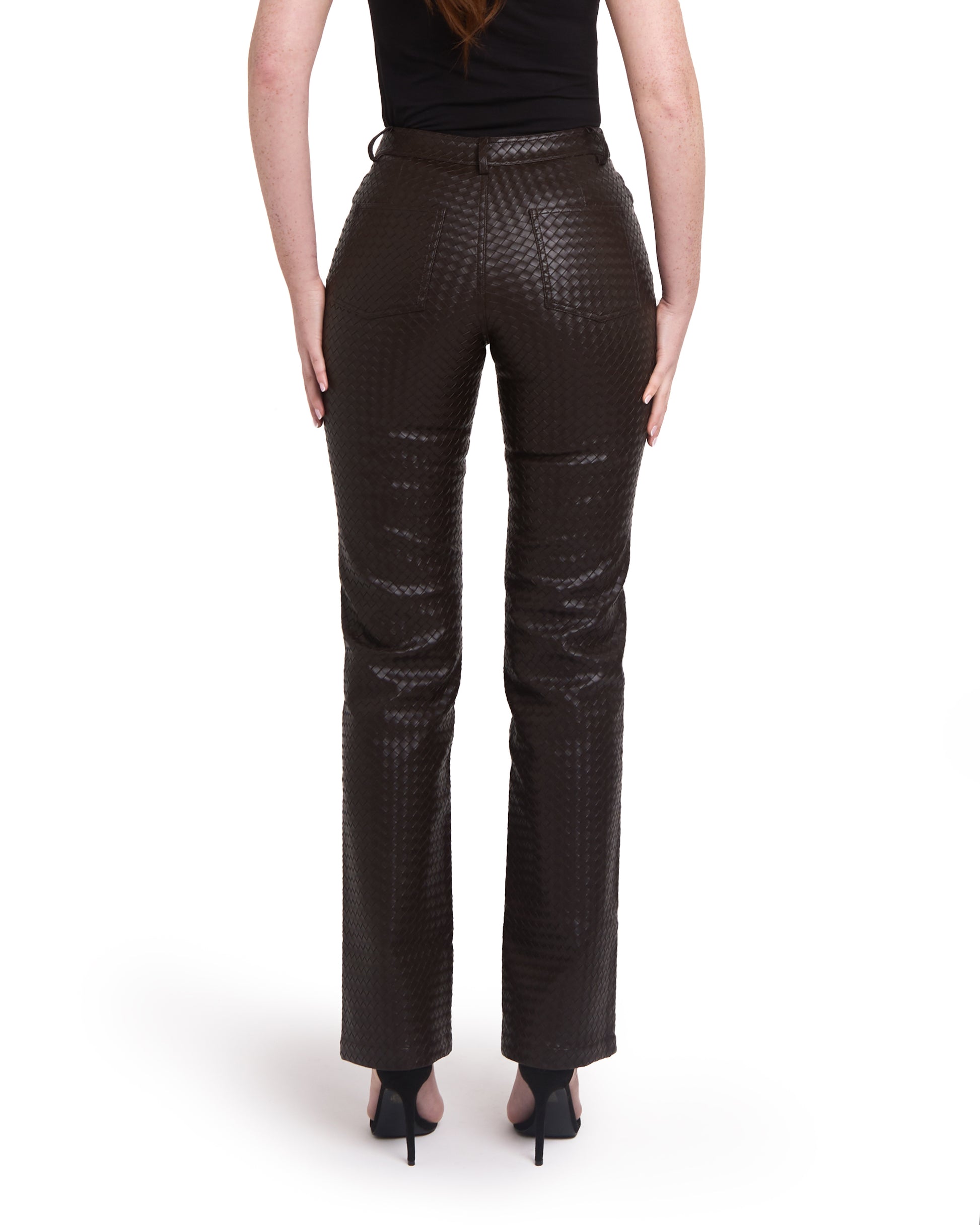 A pair of tall woven leather trousers in deep brown color, with a straight leg design. The trousers are modelled by a person standing against a plain background. Back shot